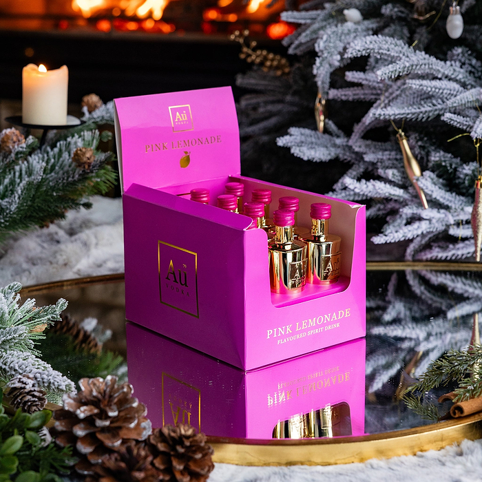 12 Au Vodka Pink Lemonade Miniature Bottles. Packaged in a Pink Box, labelled with Au Vodka Branding. Against a indoor festive background.
