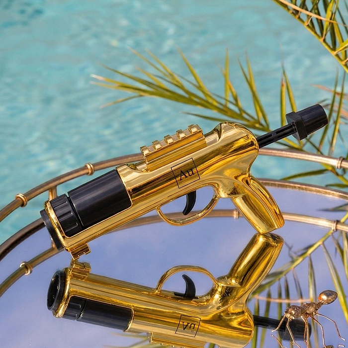 Au Vodka USA gold gun-shaped bottle on a reflective surface with a blue background
