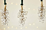 The nkuku Danvi Glass Drop Baubles - Brass & Clear (Set of 3) feature clusters of clear glass beads wrapped in brass wire and hang from a velvet tie, glowing with warm lights for a festive Christmas tree ambiance.