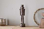 The nkuku Imay Nutcracker in antique brass stands on a wooden surface, accompanied by a silver candle holder, wreath, and bowl—creating an inviting seasonal display against a light gray wall.