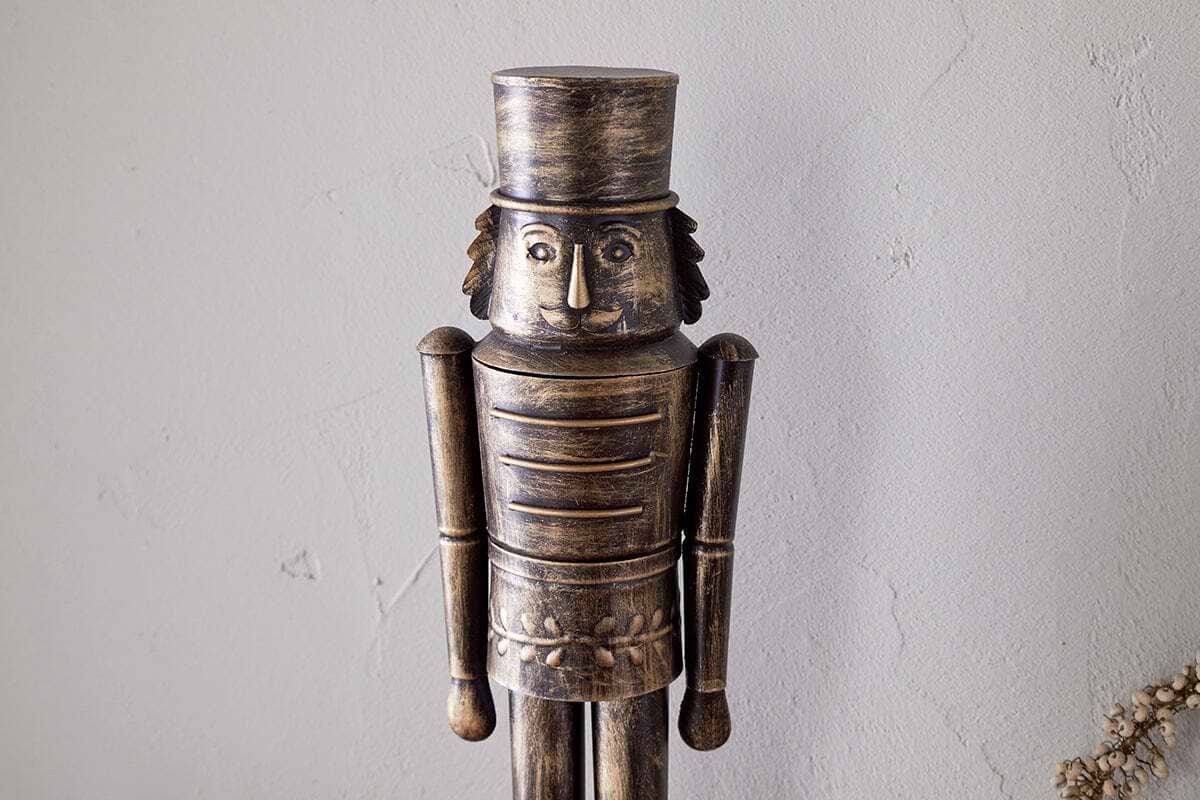 The Imay Nutcracker - Antique Brass by nkuku features a wooden soldier with a cylindrical hat, round eyes, and a mustache in a detailed uniform—ideal for festive styling or as part of your decorative nutcracker display.