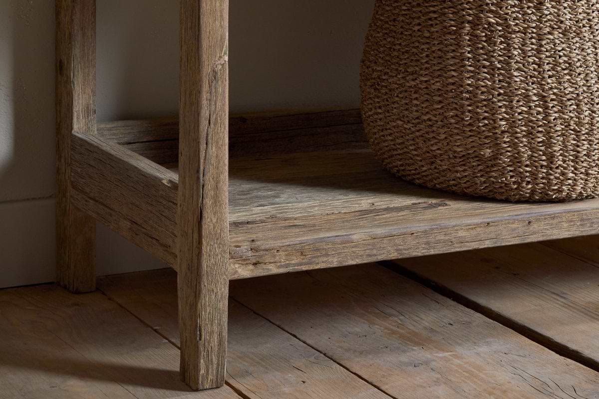 A close-up of the nkuku Ibo Reclaimed Wood Pantry Standing Shelves - Natural, featuring open shelving on a wooden floor with a woven basket on the lower shelf, showcasing its rustic wood grain and texture.