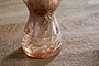 A close-up shows white onion roots spreading in water inside the nkuku Enir Hyacinth Vase—Dusty Terracotta, set on a wooden surface with a softly blurred background.