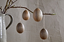 Nkuku’s Dima Mango Wood Hanging Egg Decorations (Set of 4) add minimalist, natural Easter décor when hung from a branch in a gray ceramic pitcher, set against a textured neutral-toned wall.