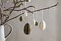 A ceramic jug holds bare branches from which nkuku’s moss green Piani Hanging Paper Decorations (set of 4) are suspended, creating a minimalist and natural Easter display against a plain beige background.