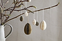 A ceramic jug of budding branches is adorned with nkuku's Piani Mini Hanging Paper Decorations in Natural & Moss, a set of 12 recycled-paper ornaments that add a minimal, natural Easter touch against a plain beige background.