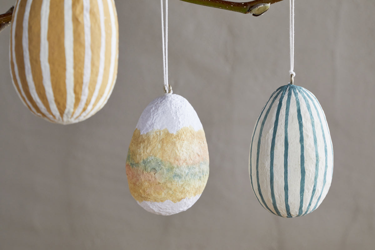 Add a charming touch to Easter decor with nkuku's Terra Hand Painted Recycled Cotton Paper Hanging Eggs—set of 3 in teal, cream, and ochre, each featuring unique hand-painted designs.