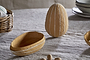 The nkuku Surya Recycled Cotton Paper Side Opening Egg in Ochre & Cream stands upright on a beige linen tablecloth—perfect for Easter tables. A matching open bowl, wicker basket, and stacked plates complete the festive scene.