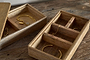 Two open Chanya Mango Wood Jewellery Boxes by nkuku sit on a rustic surface. Each natural, hand-carved box shows off gold jewellery, while light highlights the sustainable mango wood’s beautiful grain.