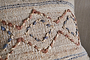 A close-up of the nkuku Nila Esha Cushion Cover - Rust & Indigo highlights textured diamond and zigzag embroidery in rust, indigo, and tan on a woven beige fabric with a neutral background.