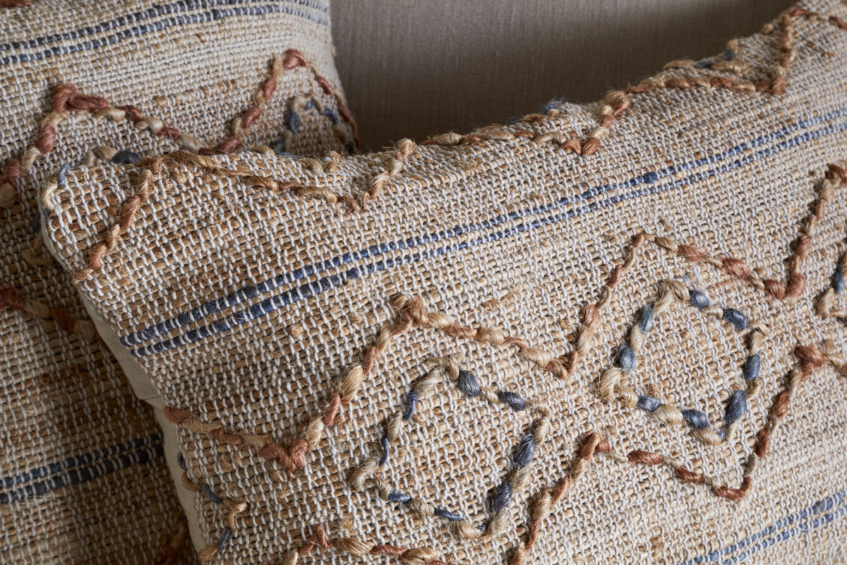 Close-up of two nkuku Nila Esha Cushion Covers in Rust & Indigo, featuring hand-embroidered geometric diamond and line motifs on coarse fabric for a rustic, artisanal look.