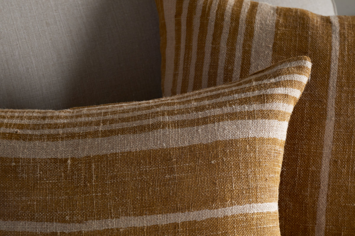 Two Eesha Jute Cushion Covers – Ochre, by nkuku, featuring a mustard yellow and off-white striped pattern on linen-like fabric, add modern rustic charm to any space.