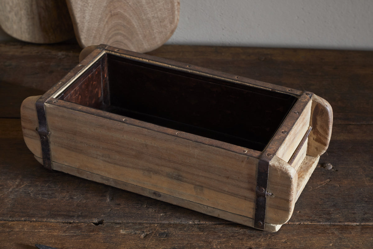 The Dudha Reclaimed Brick Box - Natural by nkuku features aged, unfinished wood and metal reinforcements. Open at the top, this rectangular storage box adds vintage, handmade charm to any rustic setting.