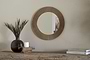 The Putali Etched Mirror - Antique Brass by nkuku hangs on a beige wall above a rustic wood console table topped with a black vase of dried grass, a white candle on wood, and stacked books for a minimal, stylish scene.