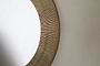 Close-up of the Putali Etched Mirror - Antique Brass by nkuku, featuring a sculptural, wide wooden frame with vertical grooves. The round mirror hangs on a light wall, reflecting a clean white space.