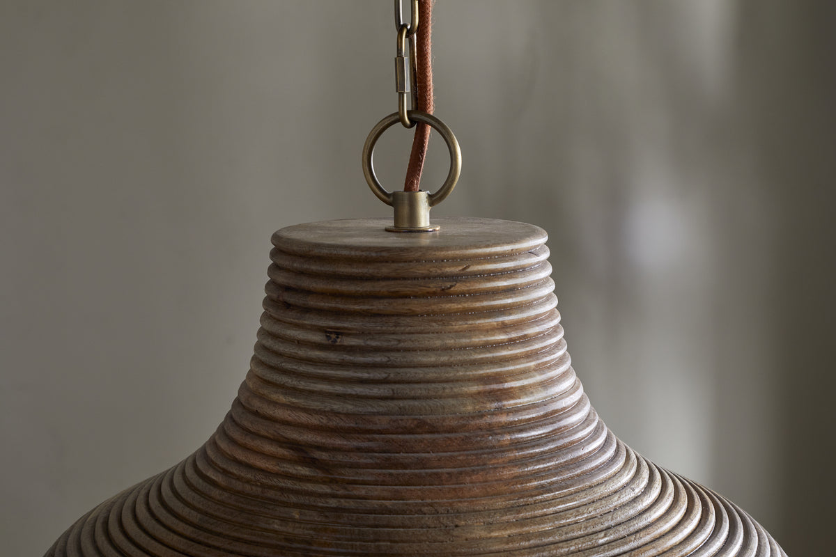 Close-up of the nkuku Nadi Grooved Wood Pendant in Natural & Antique Brass, featuring a ribbed bell-shaped shade, brown cord, and brass ring. The neutral gray background highlights its texture and functional design.
