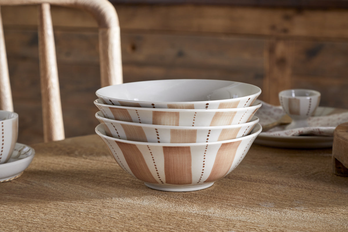 The Patthar Cereal Bowl - Cream & Clay by nkuku features hand-painted brown and beige striped and dotted designs. Stacked on a wooden table with rustic décor, these bowls add a cozy, homey touch to any dinnerware collection.