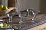 The Sooraj Champagne Coupe glasses by nkuku (set of 4) add vintage charm to a rustic table set with lemons, limes, a citrus juicer, and a bowl of salt for a casual, inviting look.