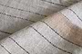 Close-up of the Buna Table Runner - Clay by nkuku, showcasing a light beige herringbone pattern with thin black stripes and a wide tan diagonal stripe. The visible fibers and natural stripes emphasize the runner’s tactile texture.