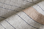 Close-up of the Buna Table Runner - Clay by nkuku, showcasing a light beige herringbone pattern with thin black stripes and a wide tan diagonal stripe. The visible fibers and natural stripes emphasize the runner’s tactile texture.