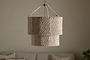 The Thimba Woven Jute Chandelier by nkuku hangs from the ceiling against a plain, light wall. Below, a neutral sofa with textured pillows adds rustic coziness and minimalist charm to the room.