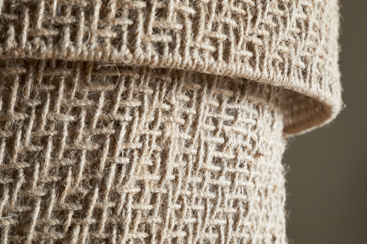 Close-up of two rolled pieces of coarse, natural beige burlap, displaying a rustic, geometric weave like the Thimba Woven Jute Chandelier by nkuku, with interlaced fibers reminiscent of its handcrafted texture under natural light.