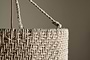 Close-up of the Thimba Woven Jute Chandelier by nkuku, showcasing its rustic texture, zig-zag pattern, and thick rope handle threaded through a metal ring. Set against a neutral beige background with gentle natural light.