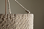 Close-up of the Thimba Woven Jute Chandelier by nkuku, showcasing its rustic texture, zig-zag pattern, and thick rope handle threaded through a metal ring. Set against a neutral beige background with gentle natural light.