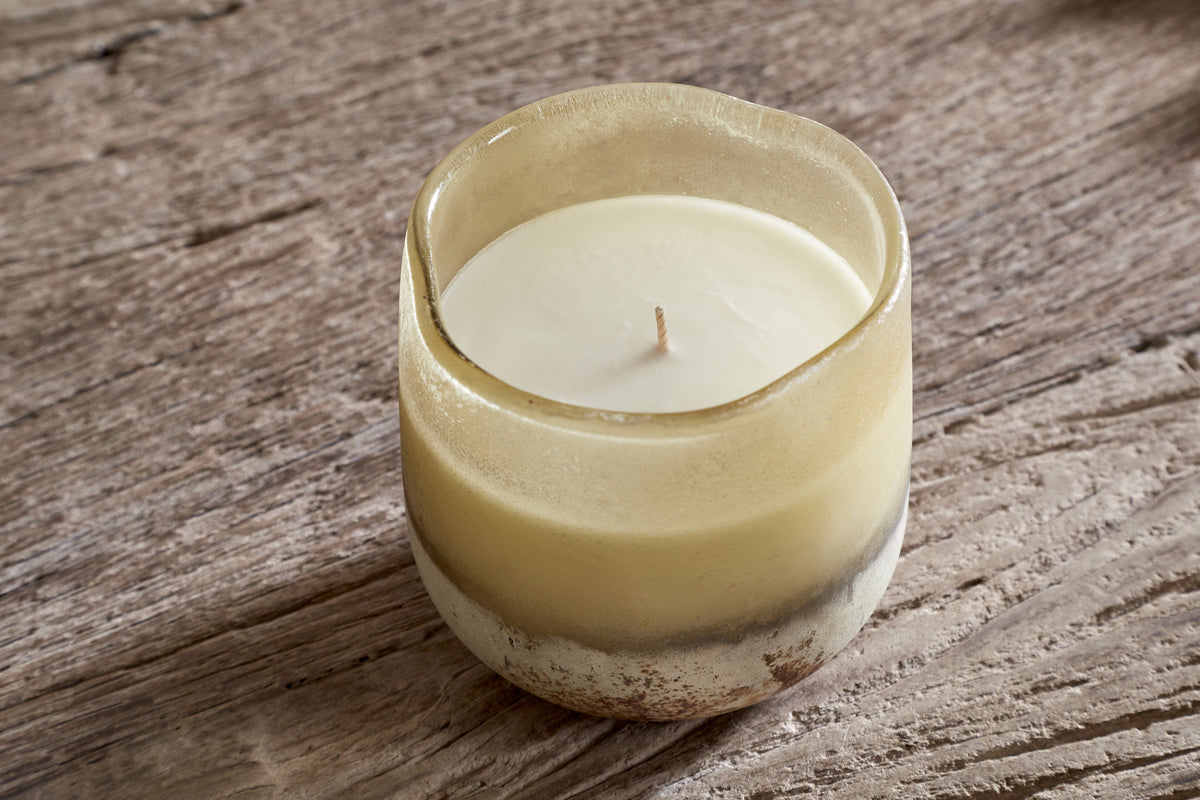 The nkuku Oakmoss & Rose 1 Wick Scented Candle in yellow features a creamy finish and sits in a translucent, slightly frosted glass holder with rustic edges, creating a cozy, natural atmosphere.