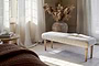 A sunlit room with sheer curtains, a round wooden table with books, and the nkuku Sanja Stripe Upholstered Bench in grey cotton at the bed’s end, plus a large vase of pampas grass on the tiled floor.