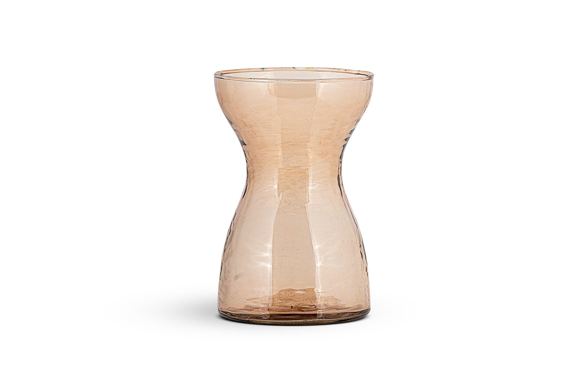 The nkuku Enir Hyacinth Vase in Dusty Terracotta features a tall, narrow, hourglass design with lightly hammered glass for a hand-blown look. Displayed on a white background, it casts a subtle shadow beneath it.