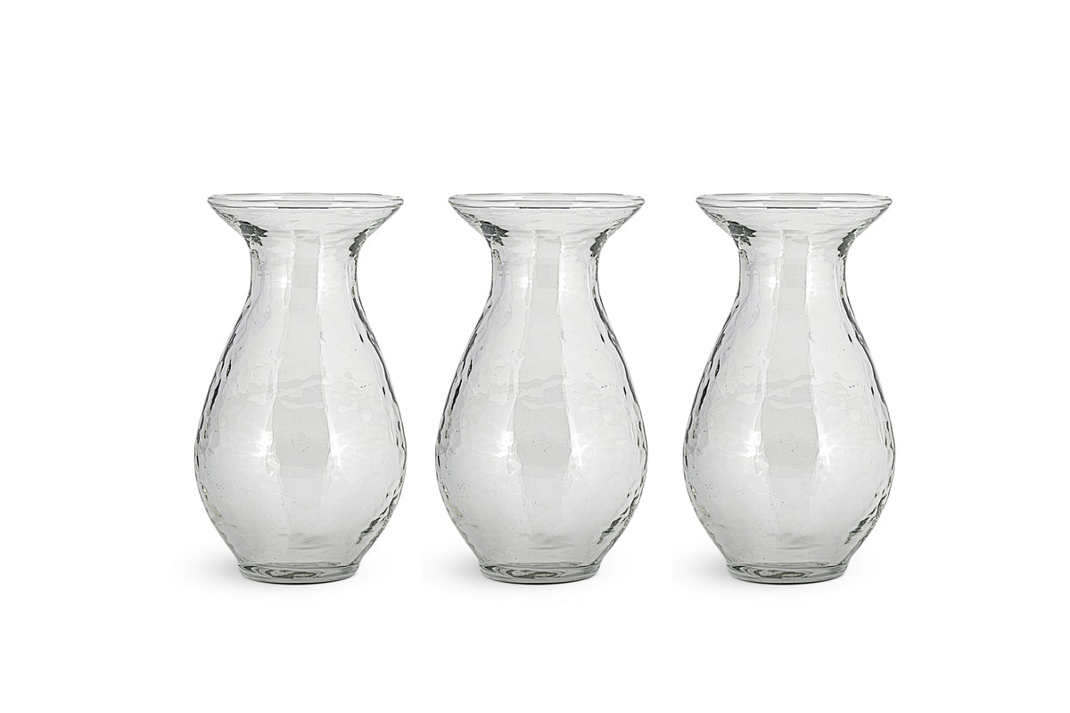 The nkuku Bapti Bud Vases – Clear (Set of 3) feature wide flared rims, narrow necks, and bulbous bodies with a textured, wavy finish. Arranged side by side, they reflect light beautifully against a plain white background.