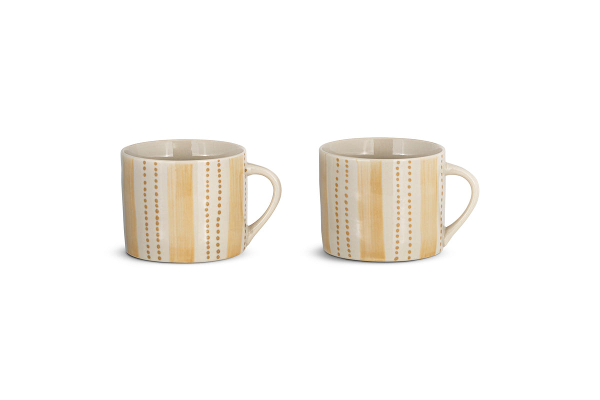 The nkuku Patthar Mug - Cream & Sand - Small (Set of 2) features two hand-painted stoneware mugs with tan stripes and dotted lines, large handles, and a glossy finish, displayed side by side on a white background.