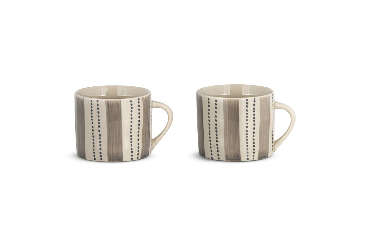 Two small Patthar Mugs by nkuku in cream and grey sit side by side on a white background. Each stoneware mug from the set of two features hand-painted vertical brown stripes with black dotted lines between them.