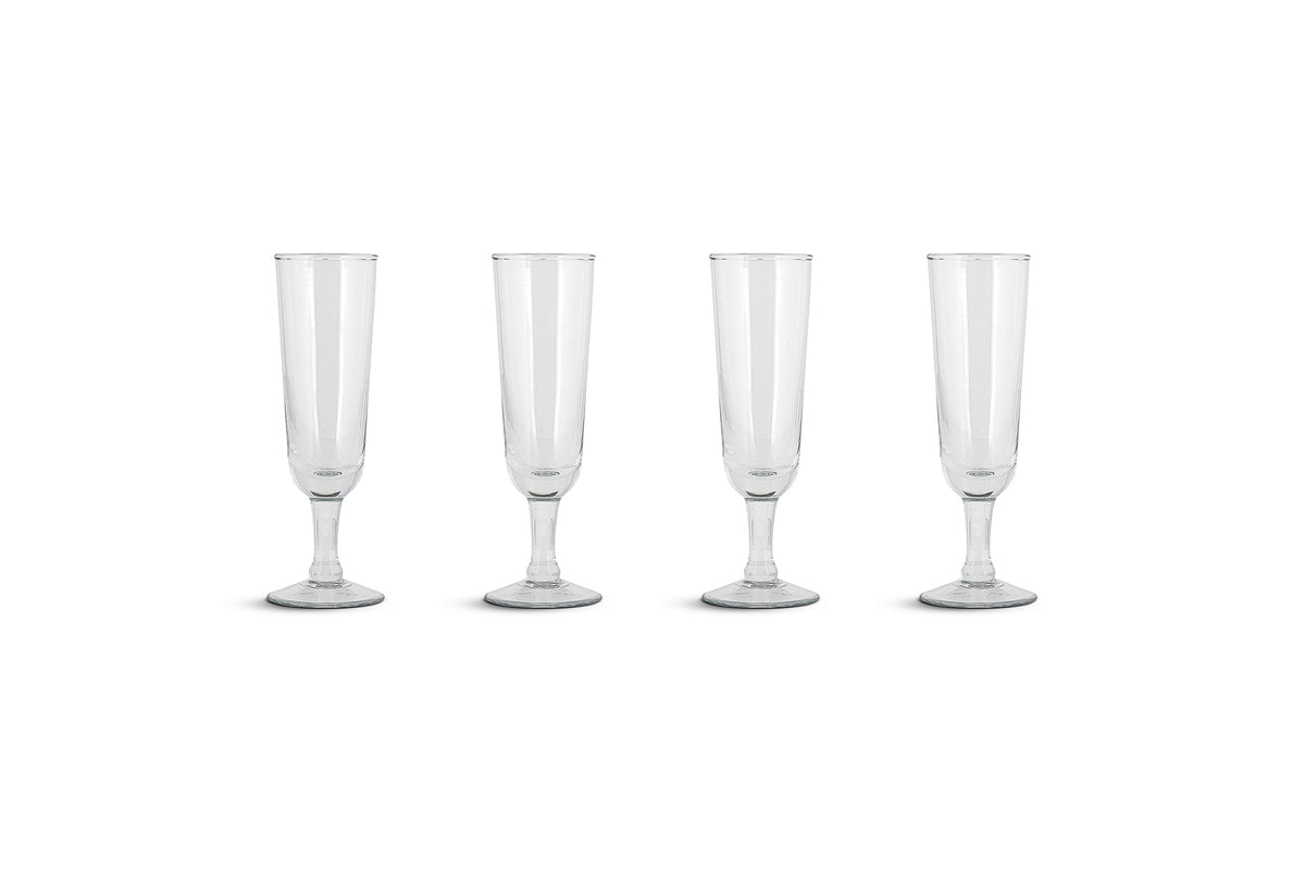 The Pani Champagne Flute - Clear (Set of 4) by nkuku features recycled glass flutes with tall, narrow bowls, slender stems, and round bases, beautifully arranged in a straight line against a plain white background.