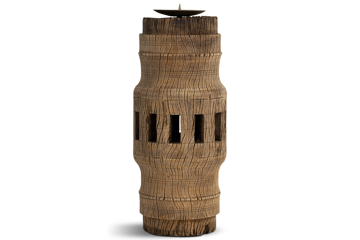 The Mvua Reclaimed Wood Pillar Candle Holder by nkuku features a tall, cylindrical shape with a weathered texture, carved vertical grooves, four rectangular center cutouts, and a small metal dish on top.