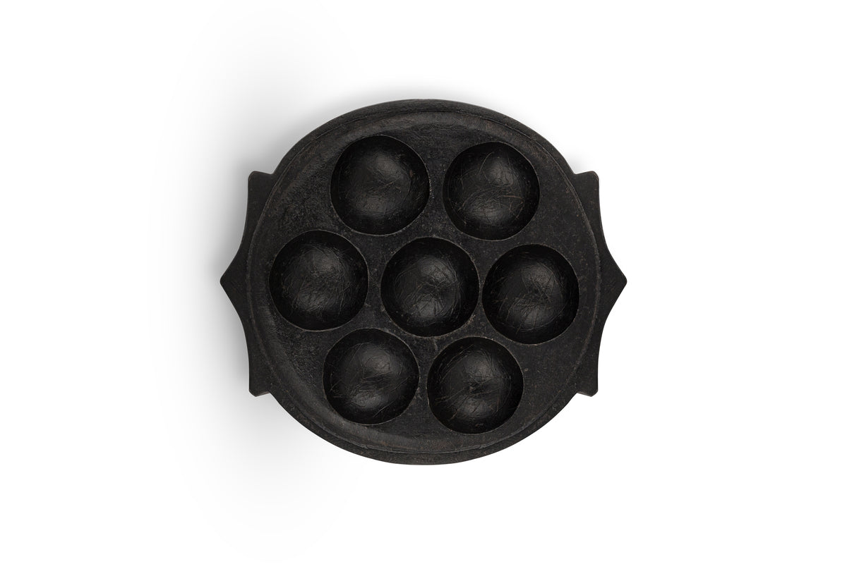The nkuku Maji Stone Multi Tealight Holder in Antique Black is an oval centerpiece with seven round indents for tealights, small side handles, and a sculptural design, shown from above on a white background.