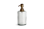 The Ilcoso Recycled Hammered Glass Soap Dispenser by nkuku features clear hammered glass, a cylindrical shape, and an antique brass pump. Its transparent, modern design stands out against a plain white background.