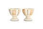 The Patthar Egg Cups - Cream & Clay (Set of 2) by nkuku feature a creamy glaze, vertical tan stripes, and dotted brown lines. Each hand-painted cup has a short, rounded base for added charm. Displayed side by side on a white background.