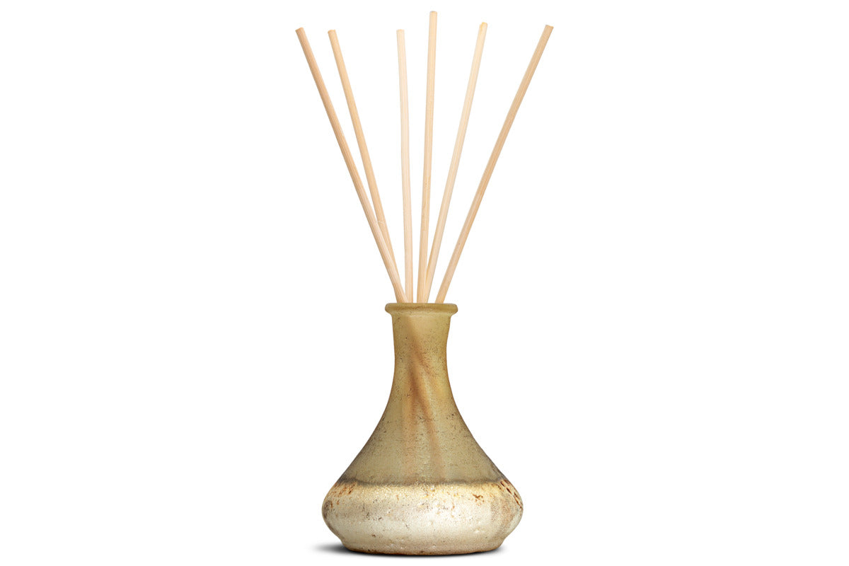 The nkuku Oakmoss & Rose Scented Reed Diffuser - Yellow features a hand-blown glass vessel with a narrow neck and gold-brown finish, infusing any room with rustic charm and a gentle floral fragrance.