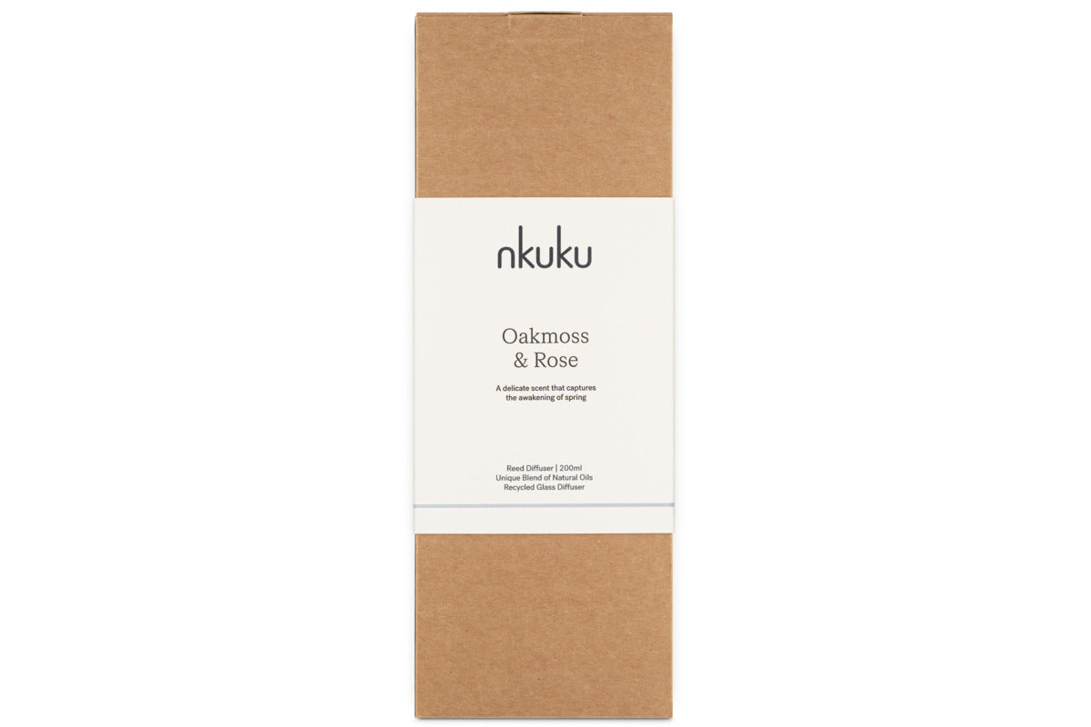 A rectangular brown cardboard box with a white band featuring the nkuku logo showcases the Oakmoss & Rose Scented Reed Diffuser – Yellow, known for its elegant floral and woody fragrance.