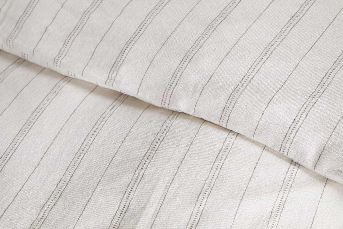 Close-up of breathable bedding with thin, vertical black stripes and a slightly wrinkled texture. Pictured is a pillow and the Anta Hemp & Cotton Duvet Cover in soothing sage green by nkuku.