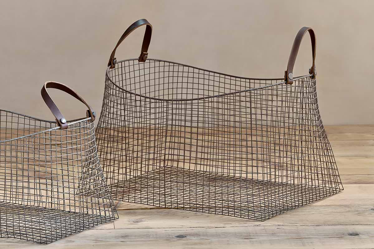 The Adah Iron Baskets - Brown (Set of 2) by nkuku feature brown leather handles and stackable storage; the larger, conical basket is open on the right, while the smaller one is partially visible on the left.