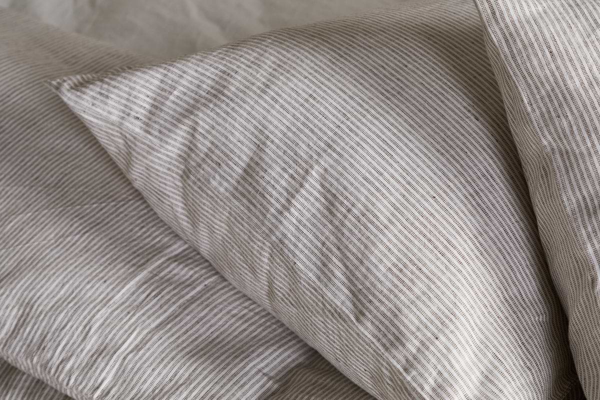 A close-up of the nkuku Borba Hemp & Cotton Housewife Pillowcases in Espresso, featuring soft, slightly wrinkled fabric with subtle stripes, resting on a matching bedsheet for a cozy and inviting look.