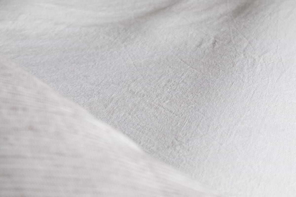Close-up of nkukus Cela Hemp & Cotton Fitted Sheet in Natural, highlighting its white, textured surface with visible fibers and gentle folds for a soft, breathable bedding look.