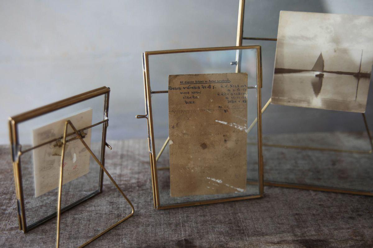 Three Danta Antique Brass Frames by nkuku display vintage photos on a textured gray surface, their hand-forged brass and glass design evoking nostalgia against a softly blurred neutral backdrop.