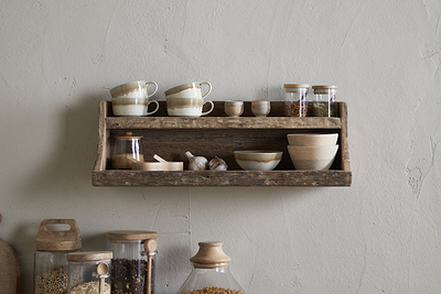 The nkuku Ibo Reclaimed Wood Storage Shelf - Natural displays cups, bowls, and jars on the wall, with larger glass jars below on the counter—all against a textured beige wall for stylish kitchen storage.