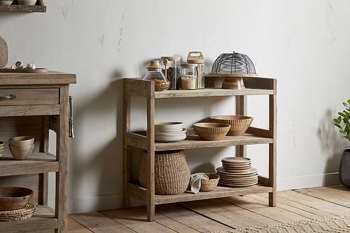 The nkuku Ibo Reclaimed Wood Pantry Standing Shelves in Natural showcase woven baskets, ceramic dishes, and glass containers in a neutral kitchen with a light textured wall and wooden floor.