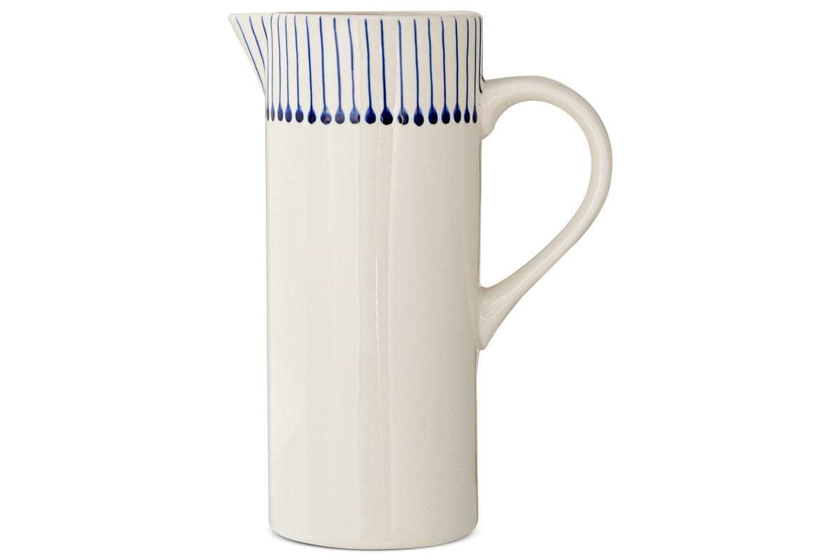 The Iba Jug - Indigo by nkuku is a tall, white ceramic pitcher featuring artisanal craftsmanship, a curved handle, narrow spout, and thin indigo lines near the rim for a modern touch.