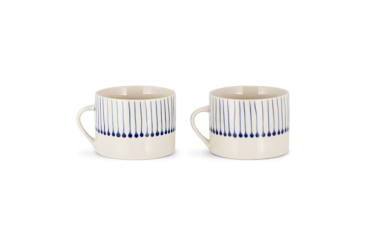 The nkuku Iba Mug - Indigo - Large (Set of 2) features hand-painted, cream-colored ceramics with vertical blue lines and dots on the upper half, showcasing a simple modern design. Both mugs have handles and are displayed against a plain white background.